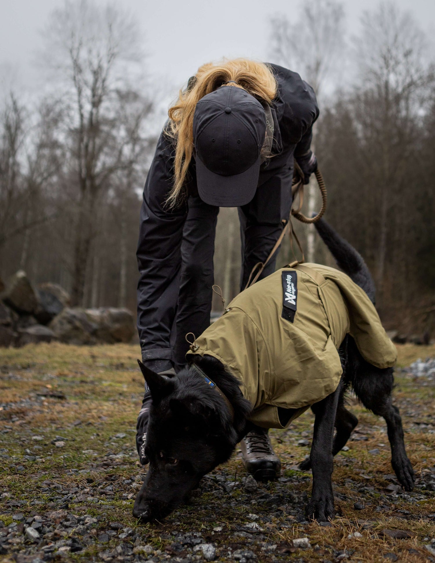 Service dog wearing Fjord raincoat while owner adjusts leash in an outdoor setting.